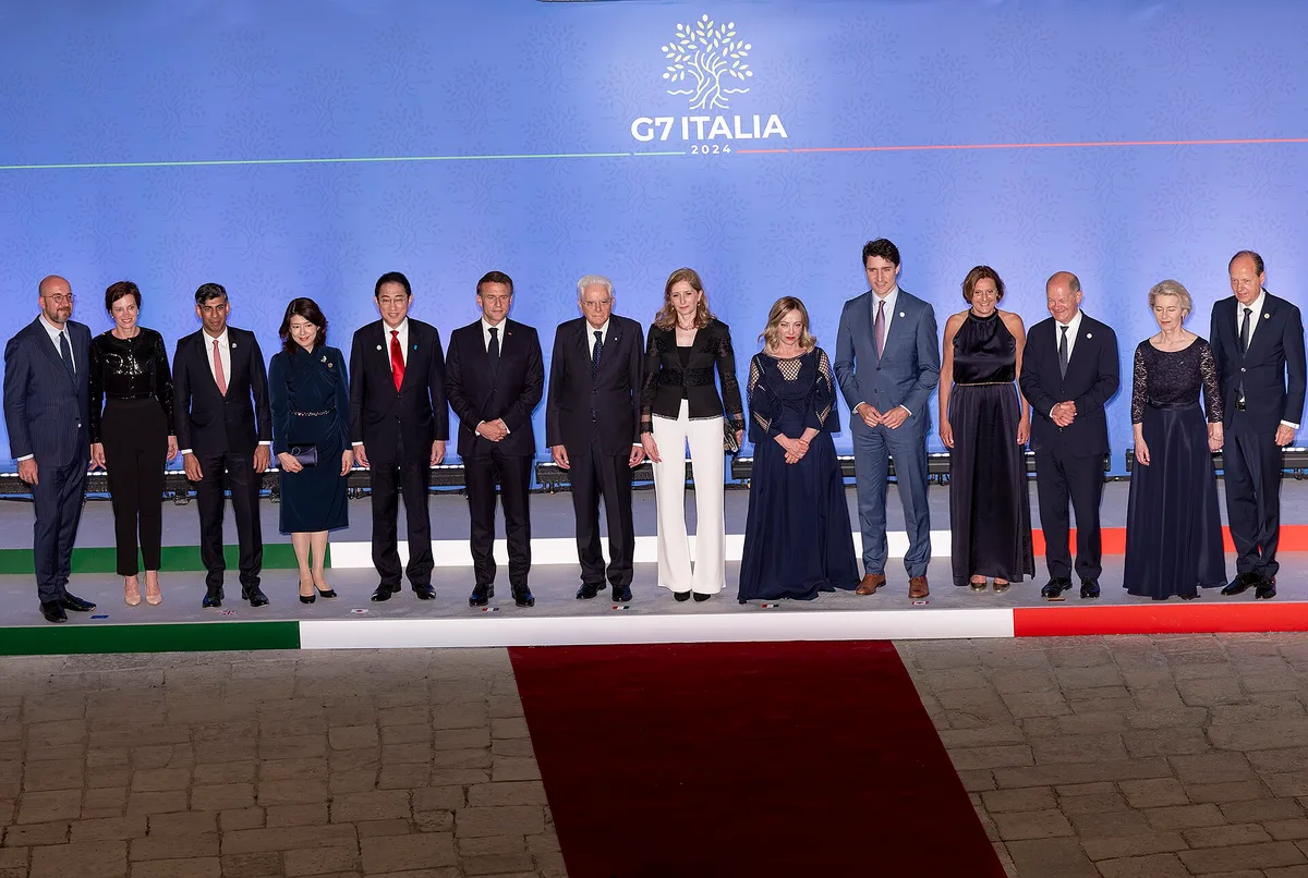 Gruppo di leader mondiali in posa ufficiale davanti al logo G7 Italia 2024 su sfondo blu, in abiti formali.